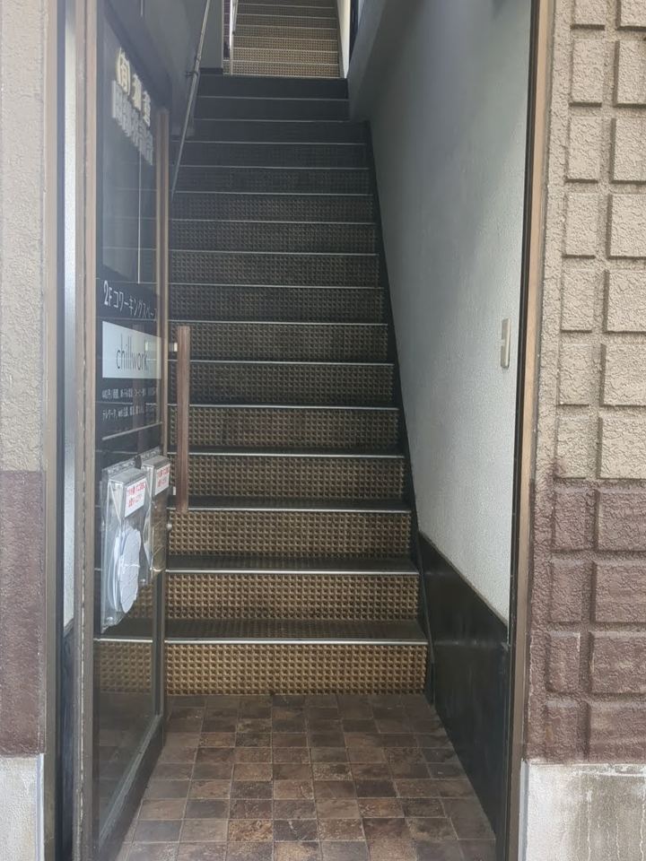 ビル1階の入口。開いた扉の奥に、2階へ上がる階段